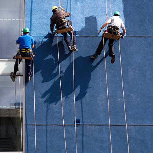 Painters recolour an office block.  Great shadow detail of painters and ropes.  Abundant copy-space.